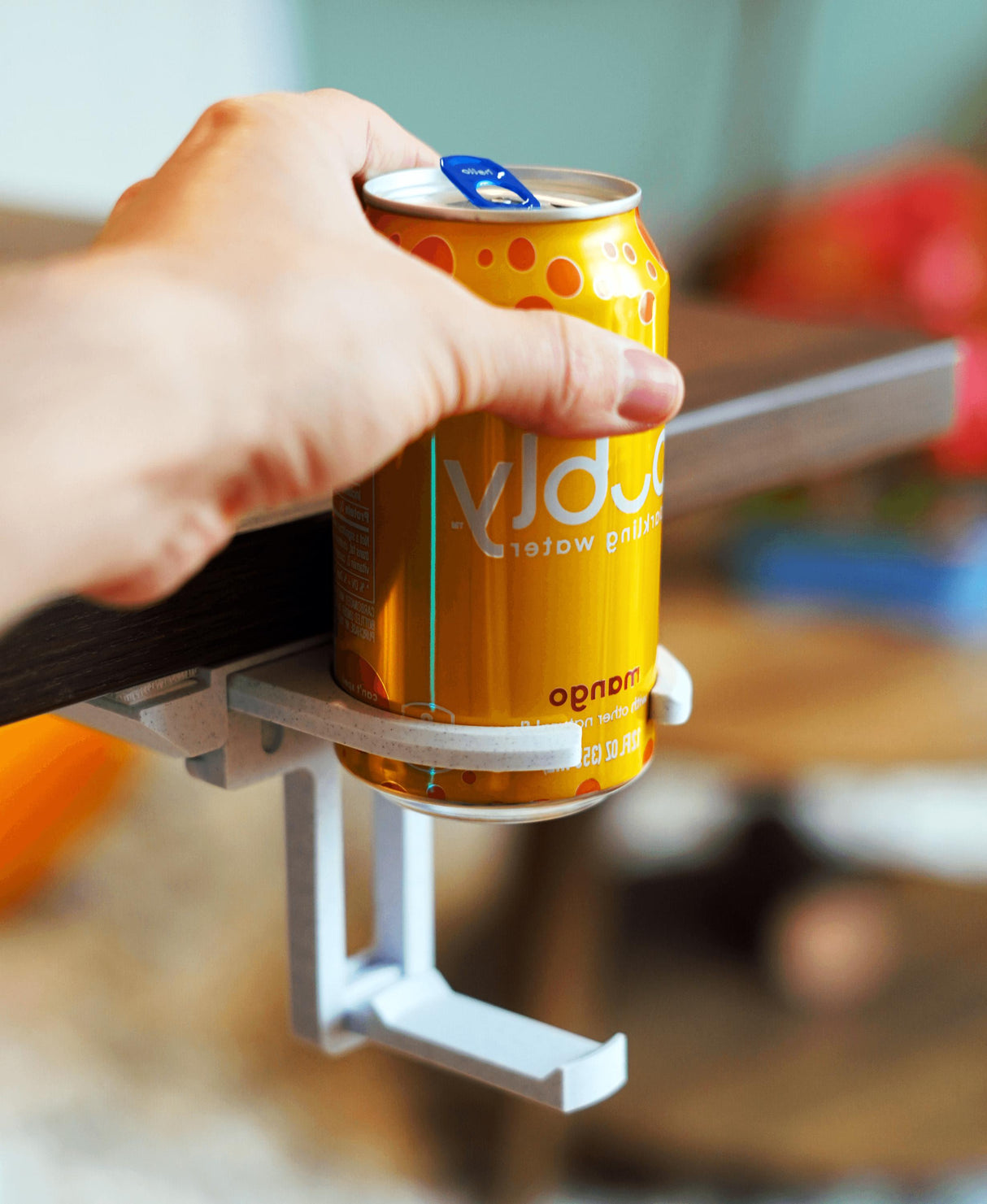 A hand holding a can of soda supported by a fold-out under desk cup holder.