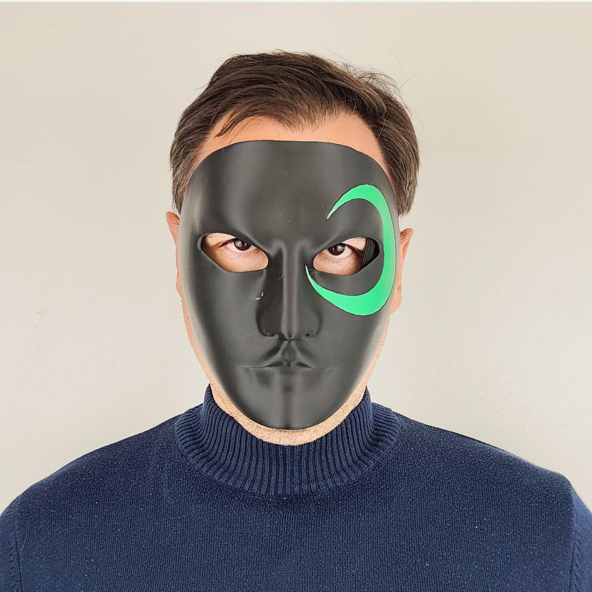 Person wearing a black 3D-printed half-face mask with a green crescent design around one eye.