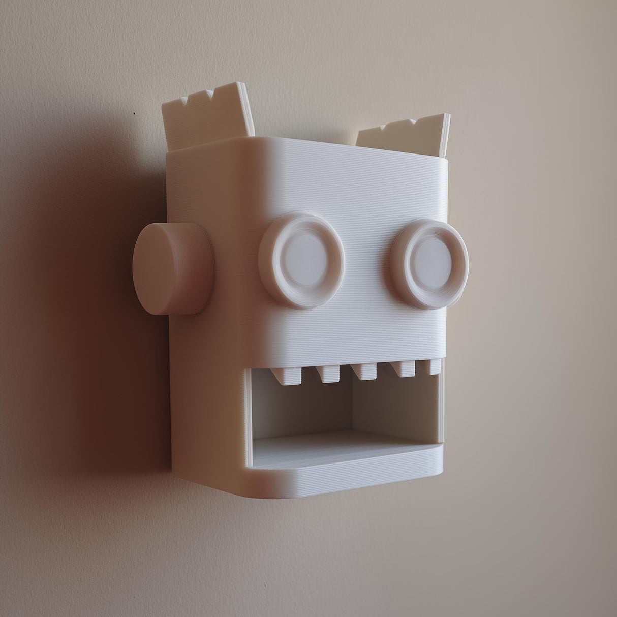 White 3D printed robot head wall organizer with an open mouth storage niche.