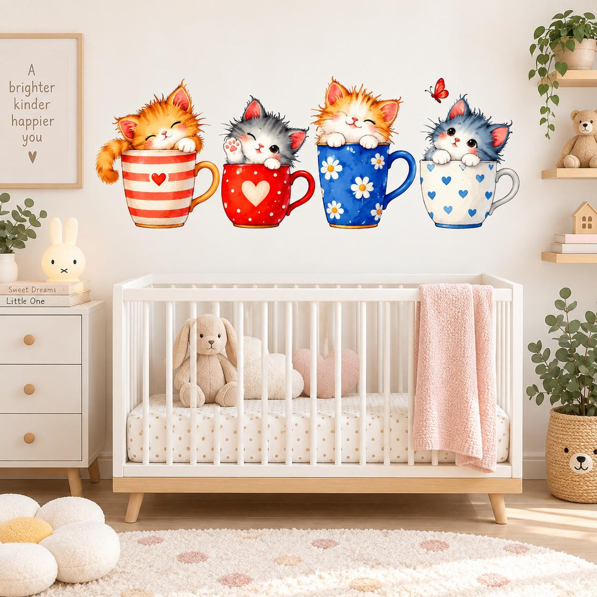 Four watercolor kittens sitting in striped, heart and daisy-patterned teacups as wall decals above a white nursery crib.