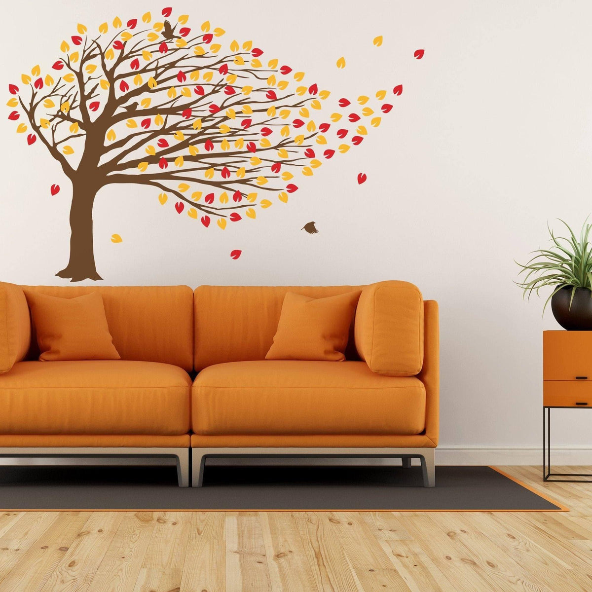 Decorative vinyl wall decal of a windy tree with colorful leaves above an orange sofa in a modern living room.