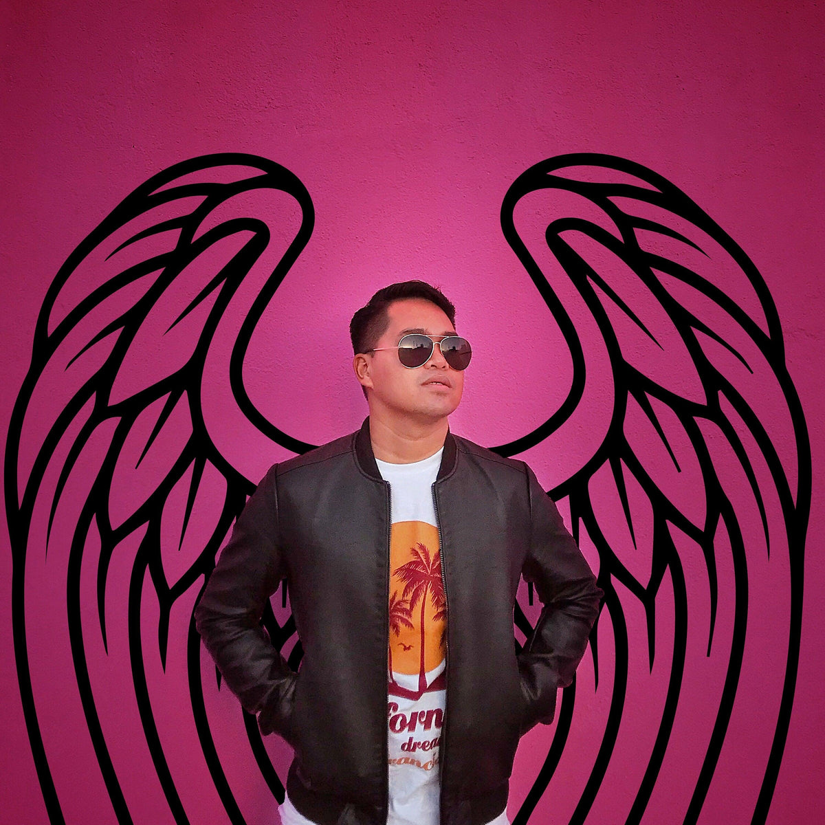 Person in sunglasses standing against a vibrant pink wall with angel wings design, showcasing stylish urban decor.