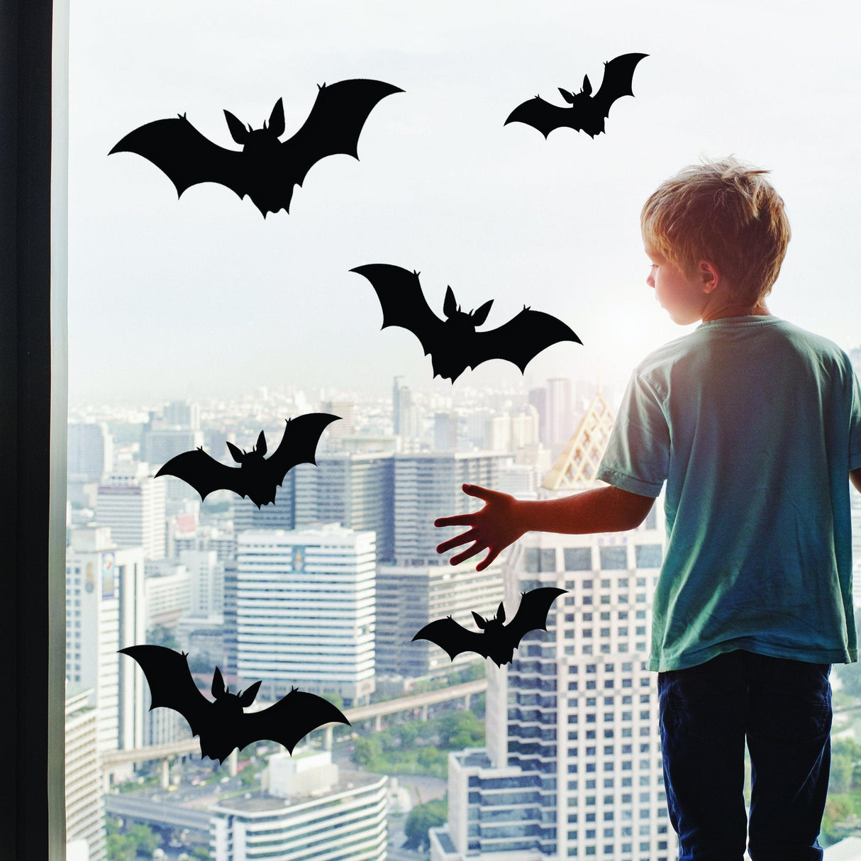 Child admiring Halloween bats window decals against a city skyline.
