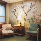 Cozy seating area with floral wallpaper and birds, featuring two chairs and a lamp.