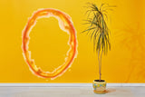 Vibrant orange portal aura wall sticker on a yellow wall with a potted plant.