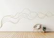 A large, abstract gold swirl line decal flows across a white wall in a minimal modern interior.