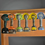 Universal cordless drill holder displaying various drill models mounted under a shelf for organized tool storage.
