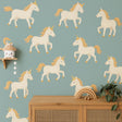 A nursery wall featuring twelve pastel unicorn decals with golden manes and horns arranged over a teal background.