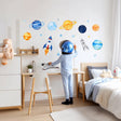 Child’s bedroom with bright watercolor space wall decals featuring planets, rockets, and stars in vivid blue and yellow.