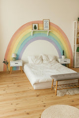 A kids’ bedroom with a large pastel rainbow wall decal behind the bed.