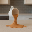 3D printed spilled espresso sculpture with a tilted cup above a broad splash-shaped base.