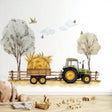 A farm-themed nursery wall decal showing a green tractor pulling a hay-loaded wooden trailer along a dirt path.