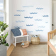 A set of blue watercolor wave decals applied randomly on a white wall in a coastal-themed kids' room with a bench.