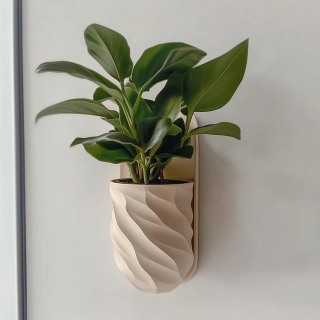 A beige, spiral-textured 3D printed planter mounted on a wall, holding a leafy green indoor plant.