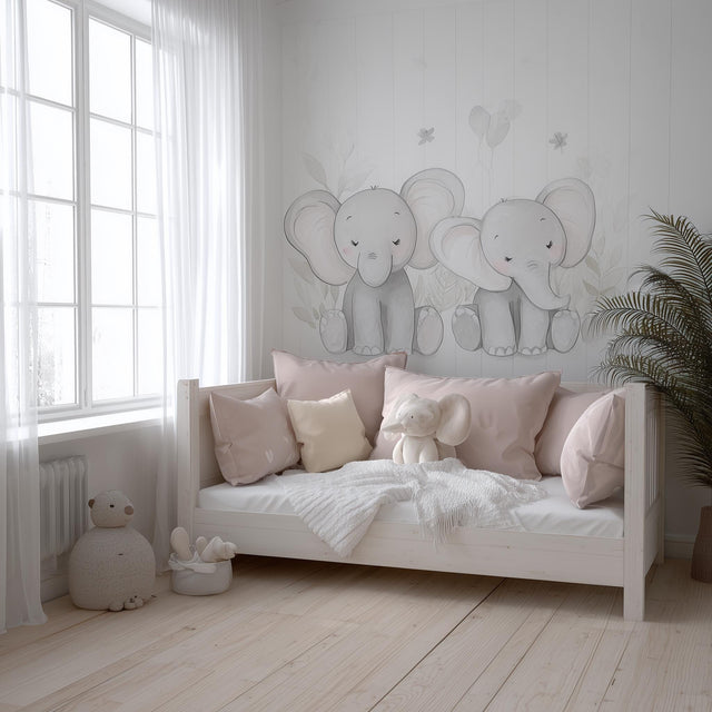A soft-toned nursery with two hand-drawn baby elephant decals on the wall above a daybed, styled with blush pink pillows.