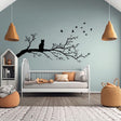 Vinyl wall decal of a cat sitting on a tree branch with flying birds.