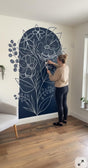 Woman applying a large floral wall decal to a white wall.