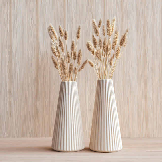 Two cream-colored origami-style vases with a pleated texture, each holding dried grasses.