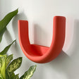 U-shaped 3D printed wall shelf mounted near houseplants in a modern interior.