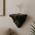 A black 3D printed wall-mounted shelf with a rugged, rock-like texture and triangular shape.