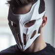 Angular white 3D printed full-face mask with narrow eye openings and futuristic contours.