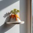 3D printed volcano-shaped wall planter on a small round shelf, with orange lava detail and a succulent plant inside.