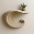 A beige 3D printed floating shelf in the shape of a curling wave.