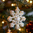 3D printed white geometric snowflake Christmas tree ornament hanging among warm fairy lights and festive decor.