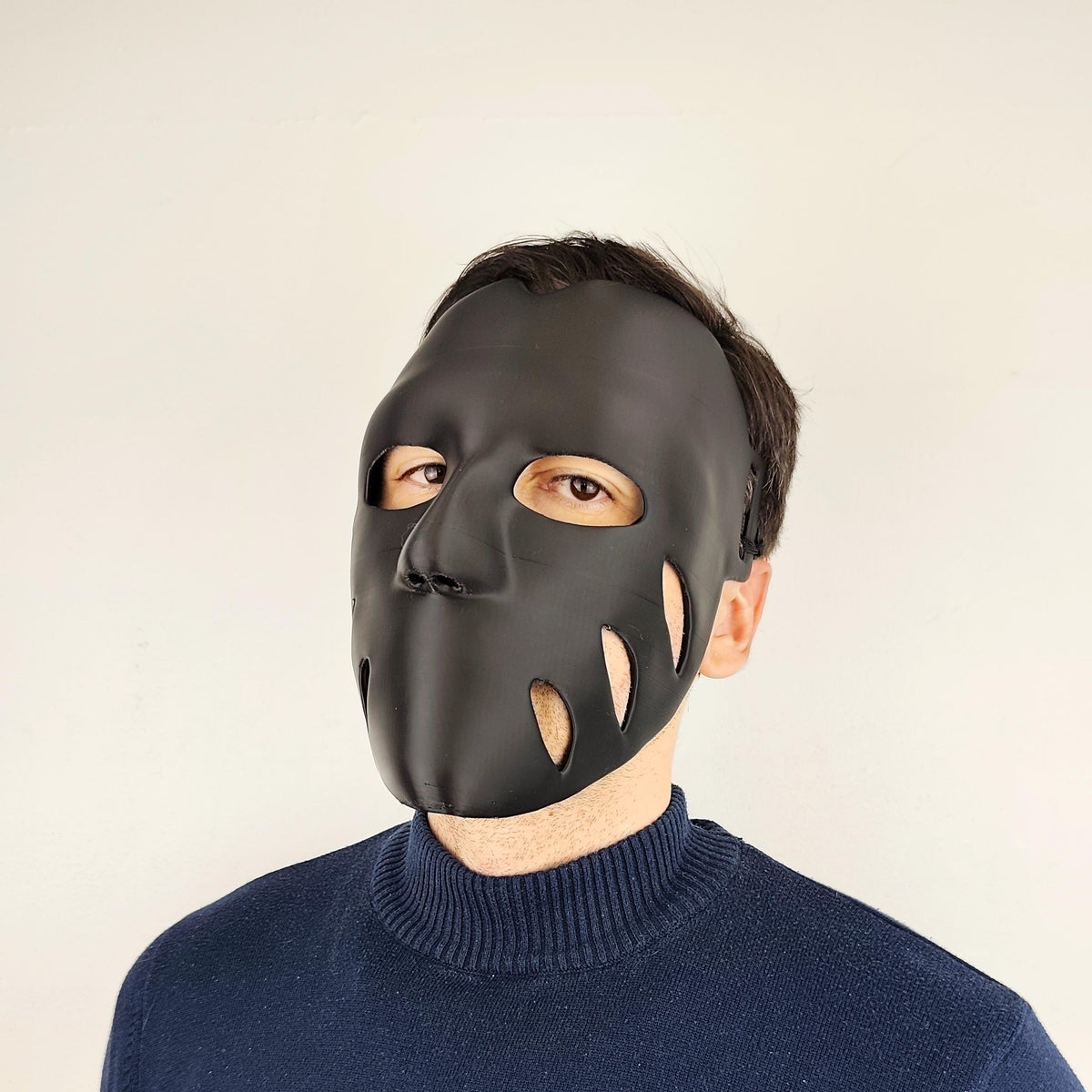 Person wearing a matte black 3D printed face mask with organic cutouts and a sleek and form-fitting shape.