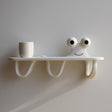 3D printed wall shelf with a smiling squiggle character and three curved hook-like legs underneath.
