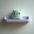 3D printed wall shelf with a small cube cat character sitting in a rounded tray-like ledge.