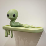 3D printed wall shelf with a long wiggly creature character on a slim ledge and dripping supports beneath.