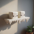 3D printed wall shelf with a dripping edge and two marshmallow-like cube characters with faces.