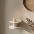 3D printed modern wall shelf in matte cream color, featuring a sculptural circular design with a candle displayed on top.