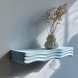 Wavy 3D printed wall shelf with a ripple-shaped support holding a decorative vase.