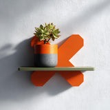 3D printed geometric X form wall shelf in orange with a green top, holding a potted plant.