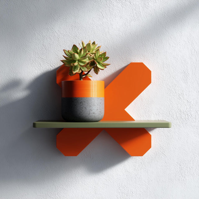 3D printed geometric X form wall shelf in orange with a green top, holding a potted plant.