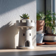 3D printed planter shaped like a small castle tower or rook, holding a succulent on a windowsill.