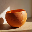 Orange 3D printed bowl shaped like a sliced basketball made from matte PLA.