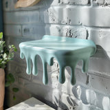 3D printed wall-mounted shelf with playful dripping "melting" design, matte pastel PLA surface.