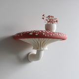 3D printed wall shelf shaped like a large red and white amanita mushroom, with sculpted gills and curved stem.