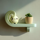 3D printed spiral wall shelf made of matte PLA plastic with a small figure and plant placed on top.