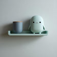 3D printed wall shelf with a slim rounded ledge holding a small blob-like character and a cup.