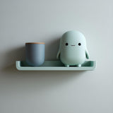 3D printed wall shelf with a slim rounded ledge holding a small blob-like character and a cup.