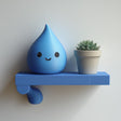 3D printed wall shelf with a small water drop character and a plant pot on a slim rectangular ledge.