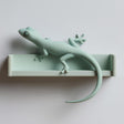 3D printed matte PLA wall shelf with an integrated gecko figure stretched along the ledge.