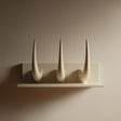 3D printed wall-mounted shelf with three tall curved horns rising from a back panel in matte PLA.