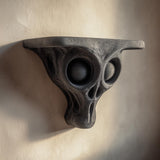 3D printed dark gray alien skull wall shelf with large hollow eye sockets and a flat floating ledge.