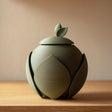 3D printed pet cremation urn with layered leaf-shaped panels and a small leaf lid handle.