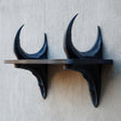 3D printed dark fantasy wall shelf supported by two curved dragon horn sculptures.